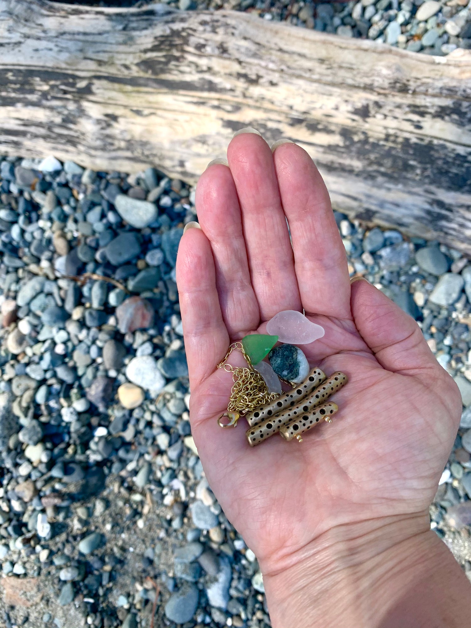 Sea glass, rock and necklace in hand at beach