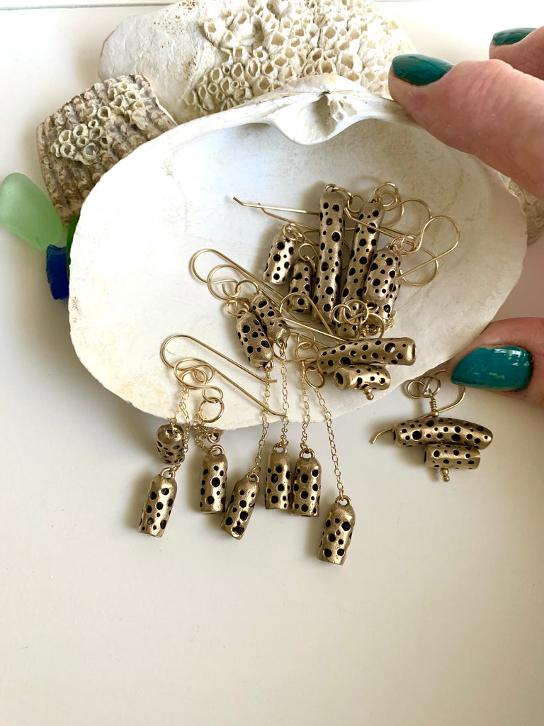 woman picking up seashell with bronze earrings